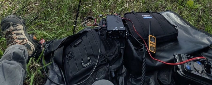 Portable RaDAR-style setup laid out in the grass: backpack, handheld transceiver, and battery pack