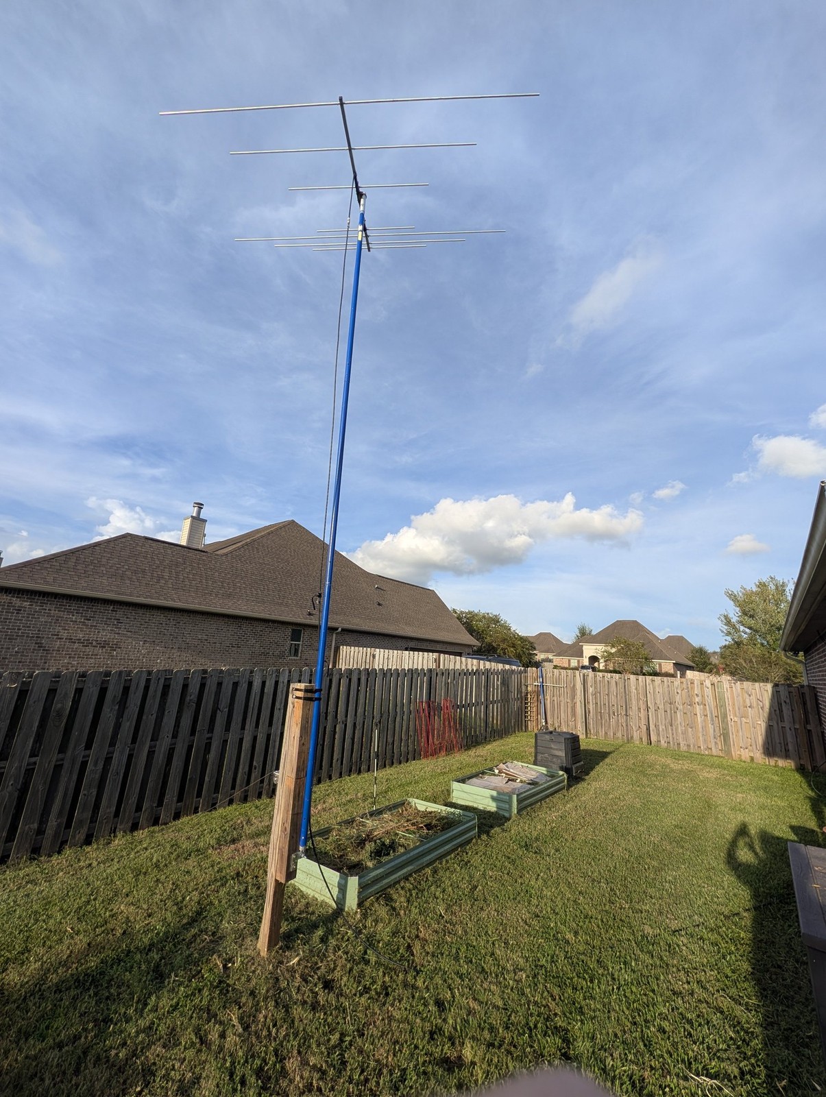 Homebrew VHF Yagi antenna on a tilt-over mast mounted to a wooden fence post in the side yard