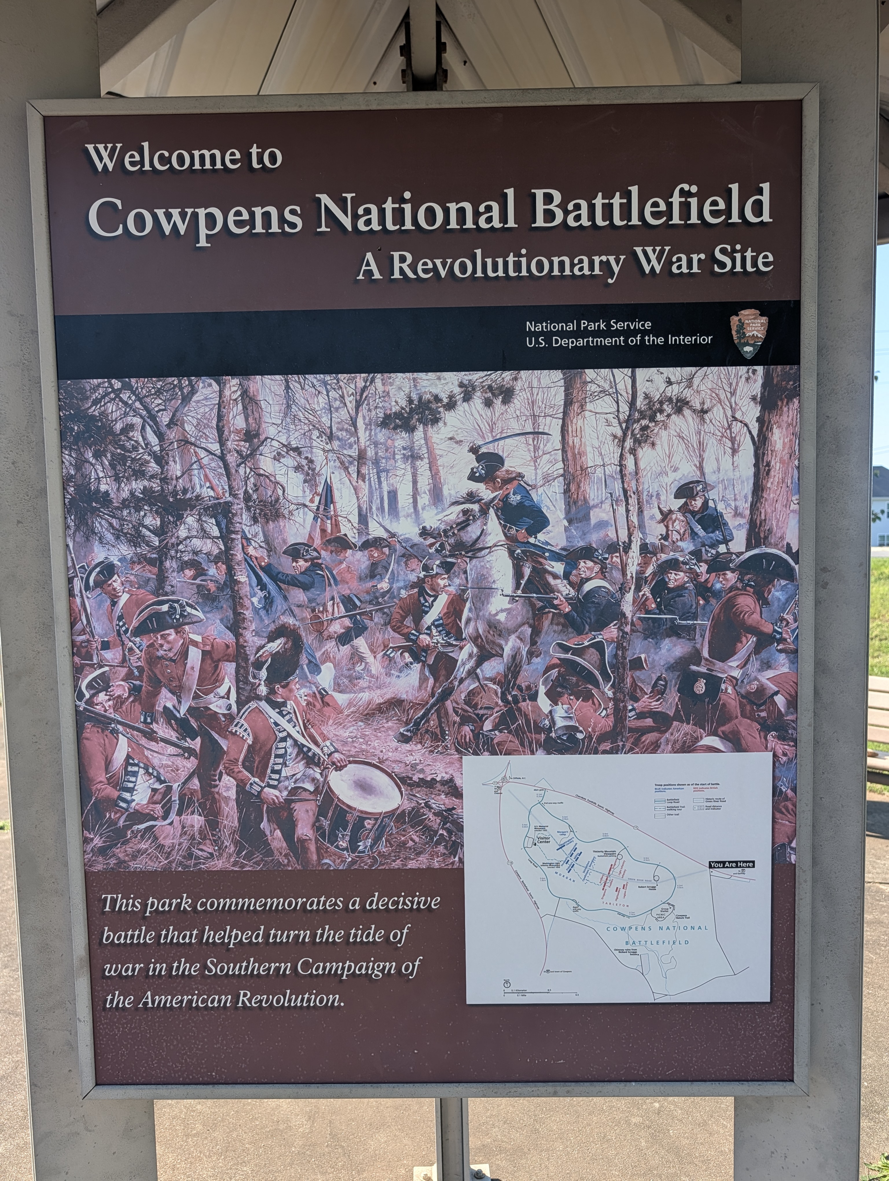 Welcome sign at Cowpens National Battlefield, a Revolutionary War site, with a painting of the battle and a park map